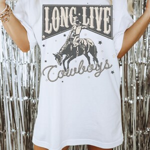 May include: White oversized t-shirt with a graphic print of a cowboy riding a bucking horse. The graphic has the text "Long Live Cowboys" in a vintage style.