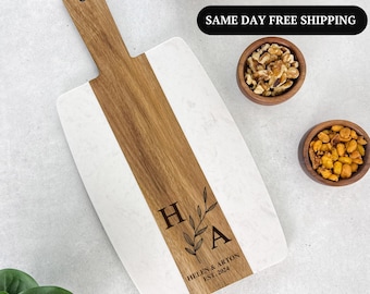 May include: A rectangular serving board with a wooden handle and a white marble surface. A central wooden stripe runs down the board. The board is engraved with the initials "H A", a sprig, and the text "HELEN & ARTON EST. 2024".