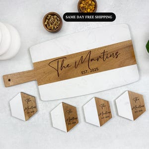 May include: A white marble and wood serving board with a wooden handle. The board is engraved with "The Martins EST. 2025". Four matching coasters are also shown, each with the same engraving.