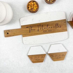 May include: A white and wood serving board with a handle, featuring the engraved text "The Matavellis EST.2025". Two matching hexagon coasters are also visible. The board and coasters are ideal for serving appetizers.