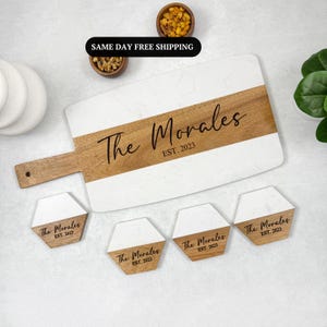 May include: A white and wood serving board with the text "The Morales EST. 2023" engraved on it. Four matching hexagon-shaped coasters with the same text are also shown.