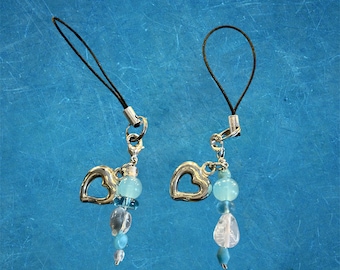 May include: Two beaded charms with silver heart pendants and a black cord loop. The charms feature a combination of clear, light blue, and opaque beads. The background is a textured blue surface.