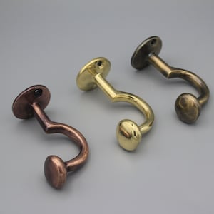 May include: Three decorative hooks in different finishes: antique brass, copper, and polished brass. Each hook has a rounded base and a curved hook.