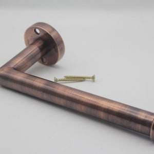 May include: A copper-toned toilet roll holder with a rounded base and a curved arm. The holder is mounted to a wall with screws.