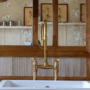 Puede incluir: Un fregadero de porcelana blanca de estilo farmhouse con un grifo dorado. El fregadero está instalado en un gabinete verde con una encimera de madera.