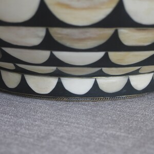 Puede incluir: Un cuenco decorativo con un dise&ntilde;o festoneado. El cuenco presenta bandas alternas de negro y blanquecino, con un ribete met&aacute;lico en la base. El dise&ntilde;o recuerda un patr&oacute;n de olas.