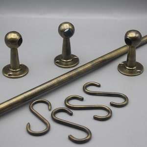 Peut inclure: Un ensemble de tringles à rideaux en laiton antique, comprenant une longue tringle cylindrique, trois supports assortis et des crochets en forme de S. Les supports ont un dessus rond. L'ensemble est conçu pour suspendre des rideaux.