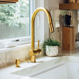 May include: A gold kitchen tap with a single lever handle and a white porcelain sink. A gold soap dispenser is to the left of the tap.