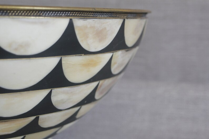 Puede incluir: Cuenco decorativo con un dise&ntilde;o &uacute;nico. El cuenco presenta un patr&oacute;n de formas negras y blanquecinas alternas, con un borde color lat&oacute;n. El dise&ntilde;o del cuenco recuerda un patr&oacute;n de concha de vieira.