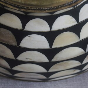 Puede incluir: Primer plano de un cuenco decorativo con fondo negro y un patr&oacute;n de medias lunas blancas y beige. El borde es dorado con un adorno decorativo.