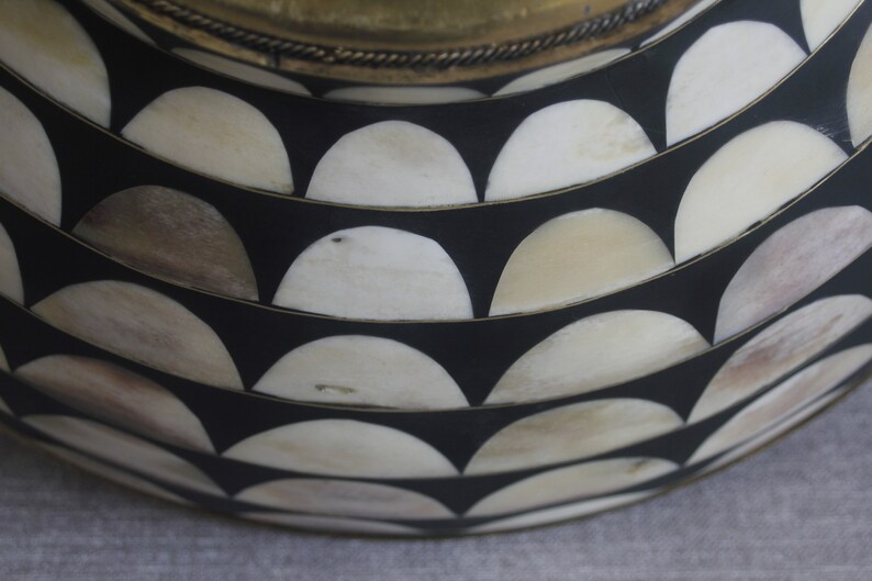 Puede incluir: Primer plano de un cuenco decorativo con fondo negro y un patr&oacute;n de medias lunas blancas y beige. El borde es dorado con un adorno decorativo.