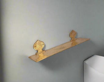 May include: A gold metal shelf with a hammered finish and decorative leaf-shaped brackets. The shelf is mounted on a light gray wall.