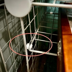 May include: Close-up of a white plastic connector joining two metal wire shelves. The shelves are part of a metal shelving unit.