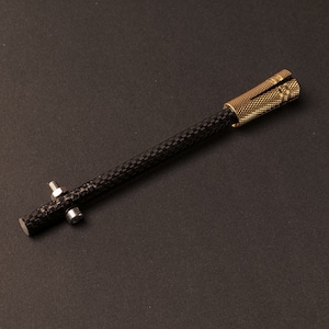 Könnte beinhalten: Ein schwarzer Kohlefaserstab mit einer goldenen Metallkappe und zwei silbernen Metallschrauben. Der Stab ist etwa 25 cm lang.