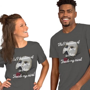 Op de afbeelding: Twee grijze T-shirts met een witte afbeelding van het Phantom of the Opera-masker en de tekst "The Phantom of the Opera is there... Inside my mind".