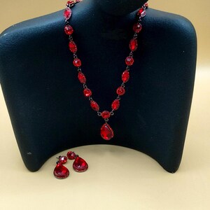 May include: A red crystal necklace and earrings set. The necklace features a teardrop pendant and the earrings are also teardrop shaped.
