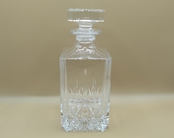 May include: A clear glass decanter with a square body and a diamond-shaped pattern. The decanter has a clear glass stopper.