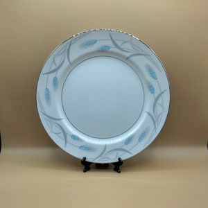 May include: A white ceramic dinner plate with a silver rim and a blue and gray wheat design.
