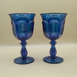 May include: Two cobalt blue glass goblets with a fluted design. The goblets have a round base and a tall stem.