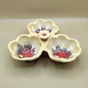 May include: A three-section ceramic serving dish shaped like flowers. The dish is cream-colored with red and gray accents. The center section is a smaller bowl.