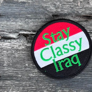 May include: A black and white round patch with the text "Stay Classy Iraq" in green lettering. The patch has the colors of the Iraqi flag.