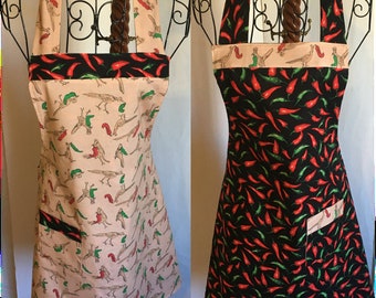 May include: Two halter aprons. One apron has a light tan background with a pattern of birds and green and red peppers. The other apron has a black background with a pattern of red and green peppers. Both aprons have a pocket and a black band with red peppers.