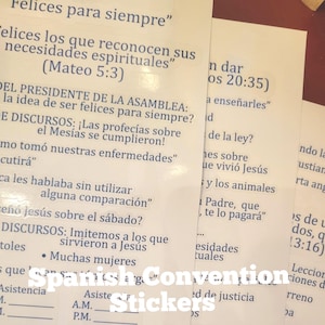May include: A stack of white stickers with Spanish text, including phrases like "Felices para siempre" and "necesidades espirituales." The stickers also feature the words "Spanish Convention Stickers."
