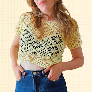 Può includere: Un top all'uncinetto giallo chiaro con un motivo floreale. Il top a maniche corte è realizzato in un materiale morbido e a trama aperta. Il top è abbinato a jeans blu.