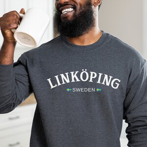May include: A dark gray sweatshirt with the text "LINKÖPING SWEDEN" in white lettering and a small Swedish flag on either side of the text.