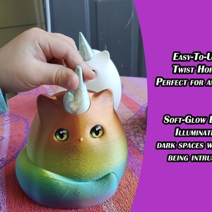 May include: A rainbow cat-shaped nightlight with a twistable horn that illuminates a room with a soft glow. The horn is being twisted by a hand.