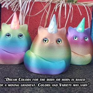 May include: Three small ceramic unicorn cat figurines with iridescent rainbow paint and a horn. The unicorn cats are sitting on a gray surface. *DREAM COLORS FOR THE BODY OR HORN IS BASED OF A MOVING GRADIENT. COLORS AND VARIETY MAY VARY*