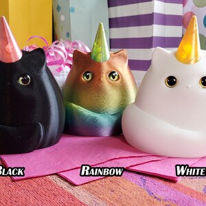 May include: Three ceramic cat figurines with unicorn horns and party hats. The cats are black, rainbow, and white.