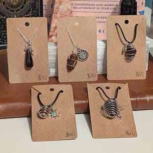 May include: Five necklaces with different crystal pendants and wire cages. The necklaces are displayed on brown paper cards with price tags. The prices are $10 and $12.