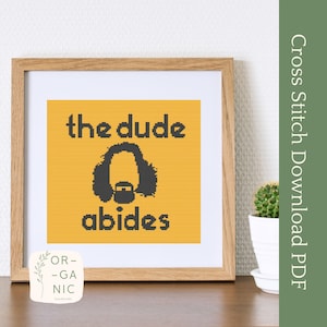 May include: Cross stitch pattern featuring a yellow background with the text "the dude abides" and a black and white silhouette of a man with long hair and a beard.