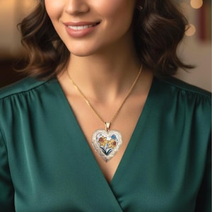 May include: A gold-colored heart-shaped locket pendant with a floral design. The pendant hangs from a delicate gold chain. The locket features yellow and blue flowers. The woman is wearing a green dress.