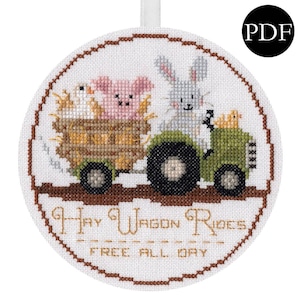 Könnte beinhalten: Runder Kreuzstich-Ornament mit einem grünen Traktor, der von einem grauen Hasen gefahren wird. Ein Schwein und ein Küken fahren in einem Heuwagen. Der Text "Hay Wagon Rides FREE ALL DAY" ist mit goldfarbenem Faden gestickt.