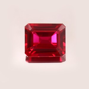 Op de afbeelding: Een gefacetteerde, rechthoekig geslepen robijn edelsteen. De edelsteen heeft een dieprode kleur met een helderroze binnenkant, die het licht reflecteert. De randen zijn nauwkeurig geslepen, wat de helderheid en schittering van de edelsteen benadrukt. De robijn staat tegen een neutrale achtergrond.