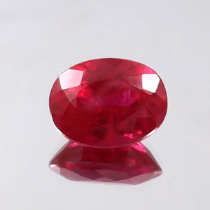 May include: A vibrant red oval-shaped gemstone with a polished finish. The gemstone is set against a white background.