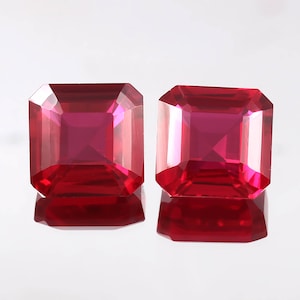May include: Two vibrant red square-shaped gemstones with a faceted cut. The gemstones are set against a white background.
