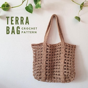 May include: A brown crocheted tote bag with long handles hangs against a white wall. The bag has a grid-like pattern and the text "TERRA BAG CROCHET PATTERN" is visible in green. Green leaves and vines are in the background.