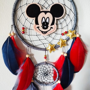 Op de afbeelding: Een grijze en zwarte droomvanger met rode en blauwe veren. In het midden van de droomvanger is een Mickey Mouse-personage afgebeeld.