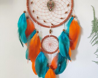 May include: A handcrafted dreamcatcher with a brown woven hoop and a delicate web design. It features teal and orange feathers, wooden beads, and a decorative metal centerpiece. This bohemian-style wall hanging adds a touch of artistry.