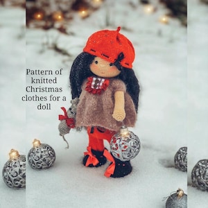 Könnte beinhalten: Eine gehäkelte Puppe mit roter Baskenmütze, braunem Kleid und roten Hosen hält einen silbernen Anhänger und eine kleine graue Maus. Die Puppe steht im Schnee mit silbernen Anhängern um sie herum.