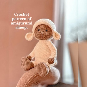 Op de afbeelding: Een handgemaakte gehaakte amigurumi schaap pop in crème en bruin. De pop heeft een witte body, een bruin gezicht en een witte hoed met oorflappen. De tekst "Crochet pattern of amigurumi sheep" is zichtbaar.