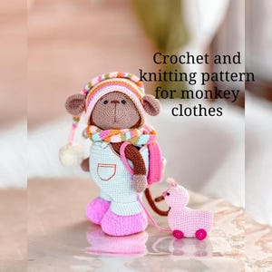 Op de afbeelding: Een gehaakte apenpop met een hoed, sjaal, overall en roze laarzen. De aap is bruin met een lichtblauwe outfit en een roze sjaal. Er is een klein roze trekdier bevestigd. De tekst "Crochet and knitting pattern for monkey clothes" is zichtbaar.