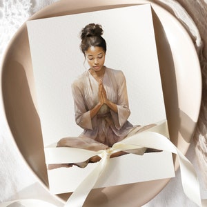 May include: A watercolor painting of a person sitting in a meditative pose with their hands clasped in prayer. The person is wearing a light brown robe and has dark hair pulled back in a bun. The painting is on a white card with a white ribbon tied around it.