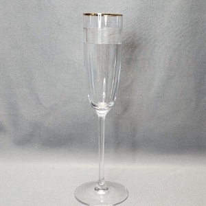May include: A clear glass champagne flute with a gold rim. The flute has a delicate, etched design around the bowl.