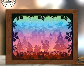Puede incluir: Una escena navideña recortada en papel con un fondo degradado arcoíris. La escena presenta a Papá Noel, muñecos de nieve, un árbol de Navidad y un trineo tirado por renos con el texto "Feliz Navidad".