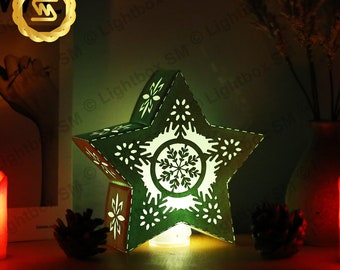 May include: A green star-shaped paper lantern with a white snowflake design. The lantern is lit from within, casting a warm glow.
