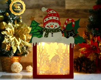 May include: A wooden Christmas light-up box features a snowman with a red and white hat, a green tree, and a candy cane. The box has a cut-out design of a winter scene with a gnome holding a gift.